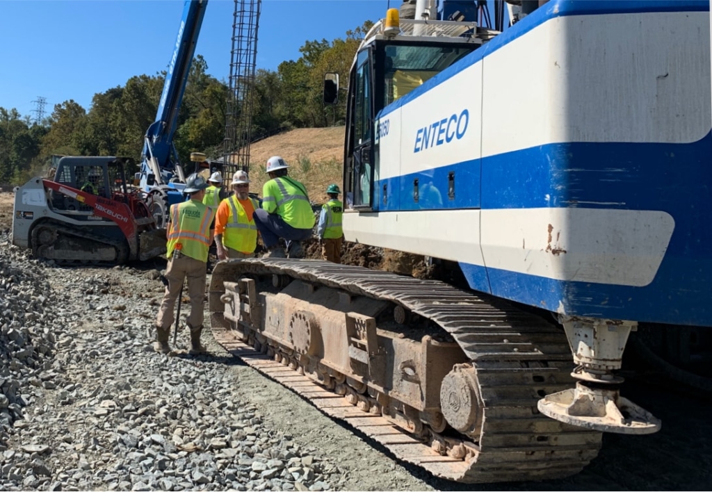 A group of construction workers standing next to a blue and white excavator.