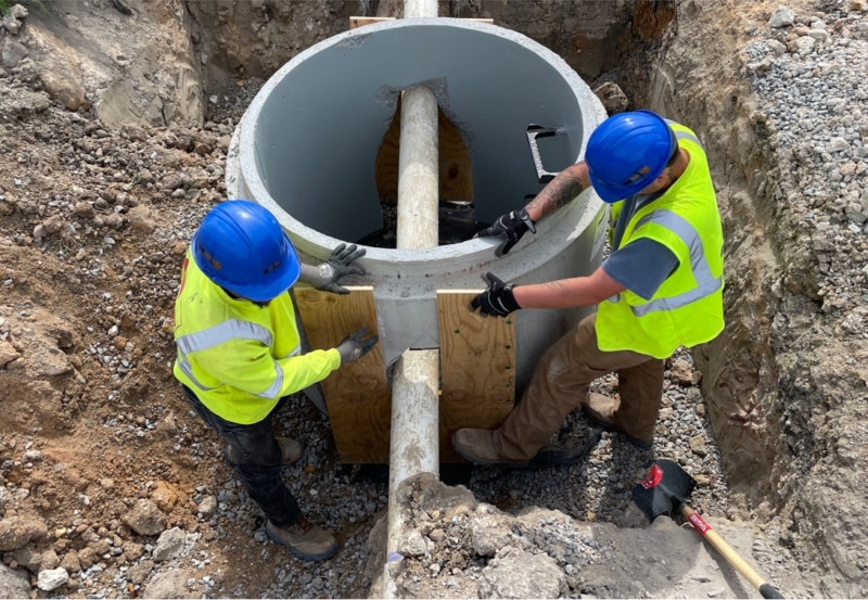 Two construction workers working on an underground pipe.