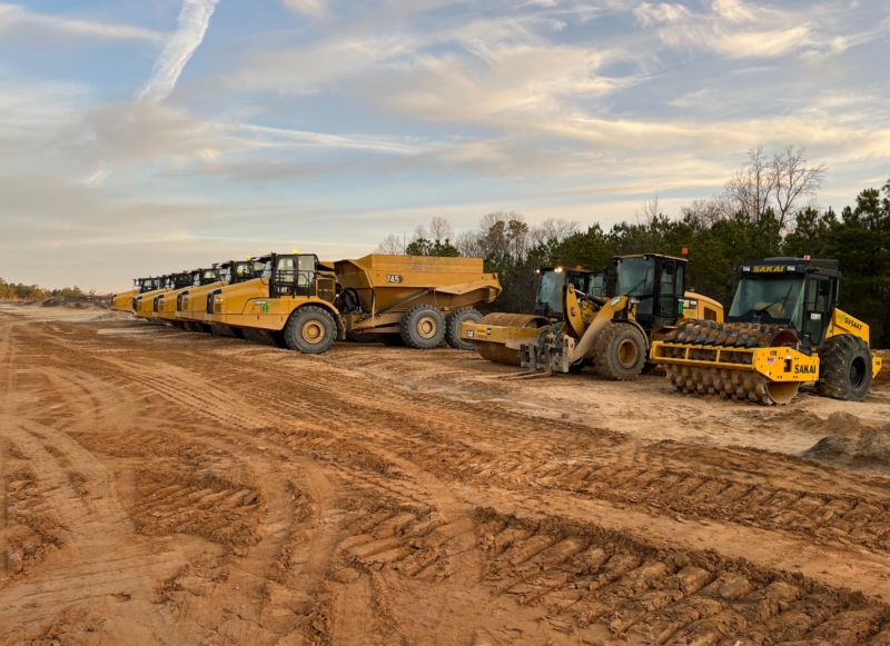 A group of heavy construction machinery parked on a dirt road.