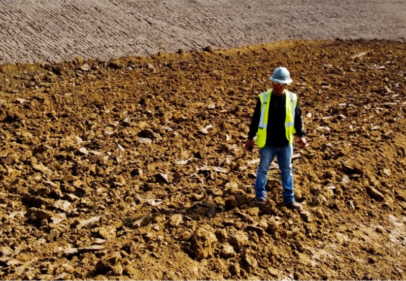 A construction worker standing in a dirt field with a shovel.