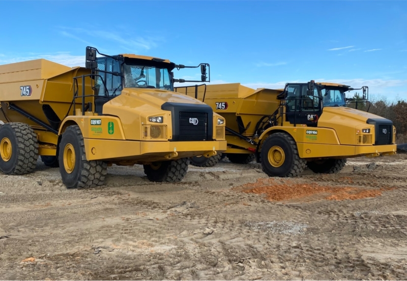 Two yellow dump trucks parked in a dirt field.