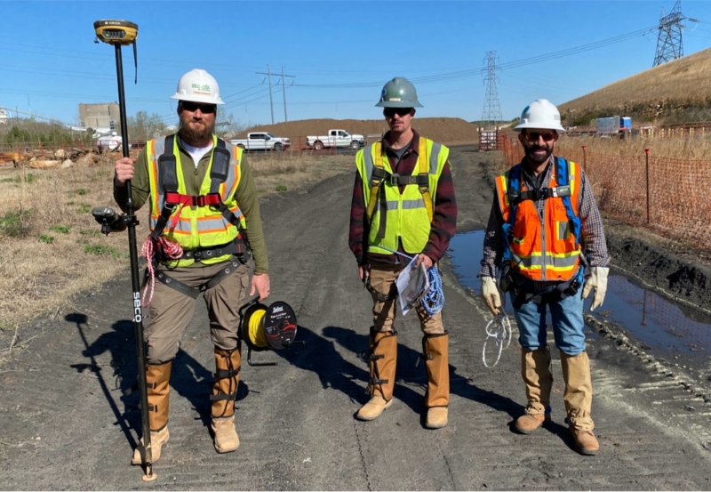 Three construction workers standing on a dirt road.