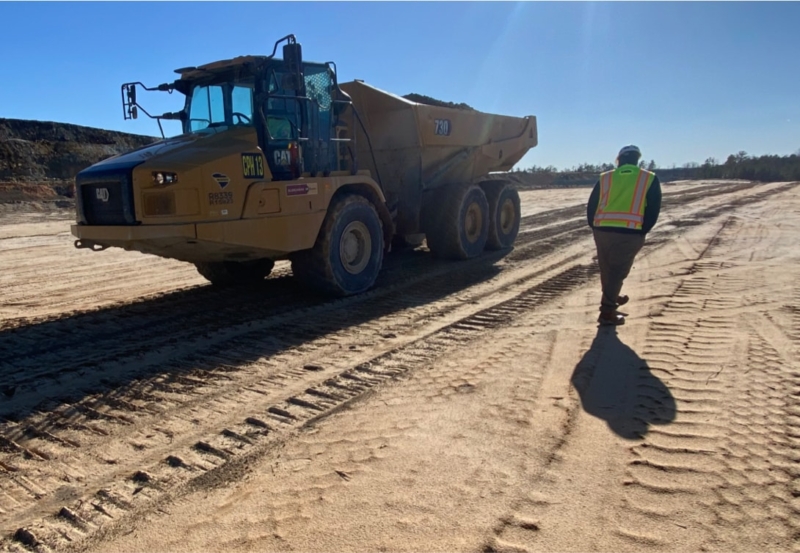 A construction worker standing next to a dump truck on a dirt road.